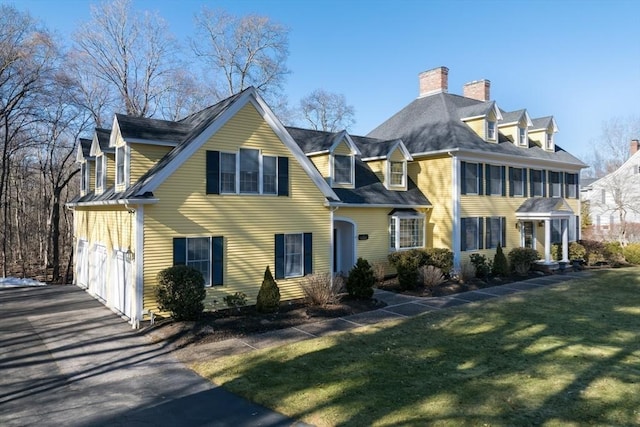 view of front facade with driveway, a front lawn, and a chimney