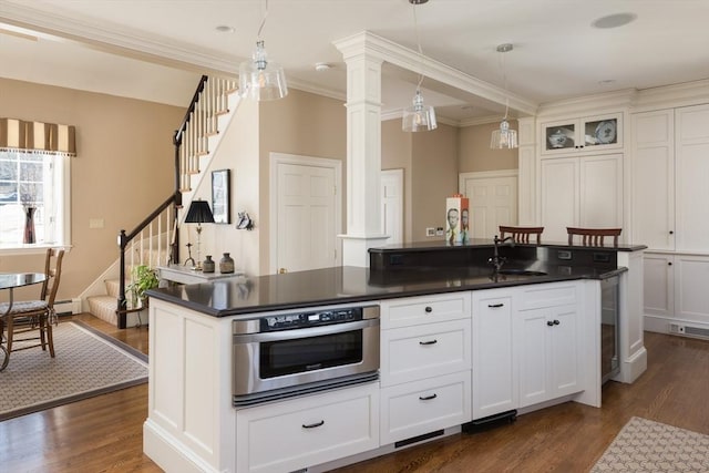 kitchen with white cabinets, dark countertops, dark wood-style floors, oven, and a sink