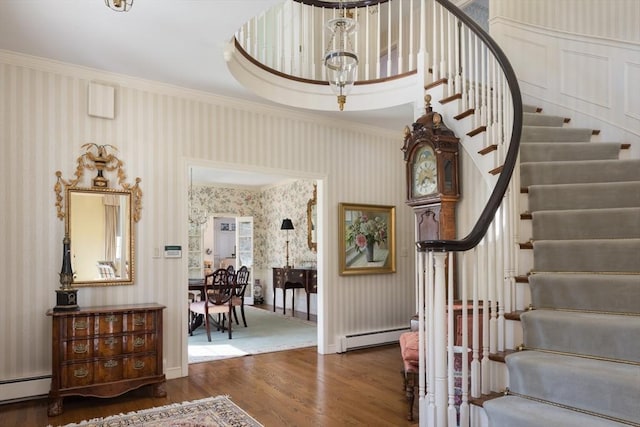 stairway featuring a baseboard heating unit, wood finished floors, ornamental molding, and wallpapered walls