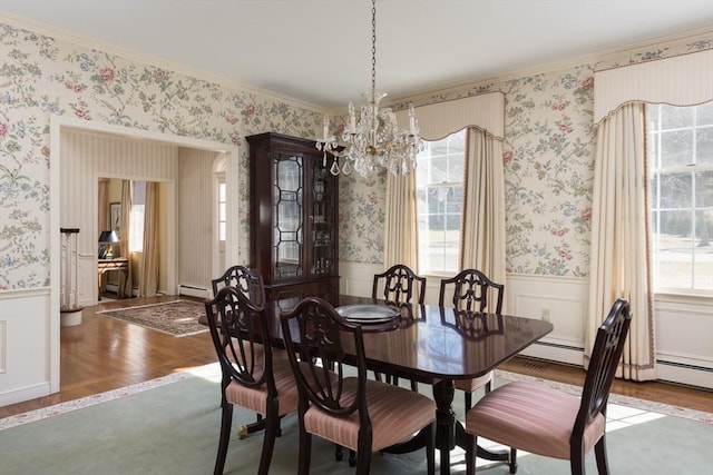 dining room with a wainscoted wall, a baseboard heating unit, wood finished floors, and wallpapered walls