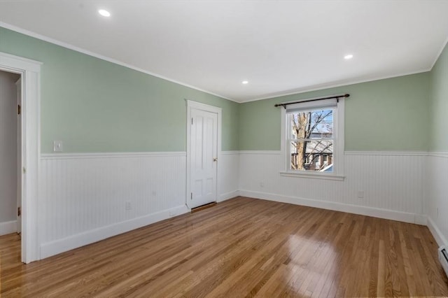 empty room featuring light hardwood / wood-style floors, a baseboard heating unit, and crown molding