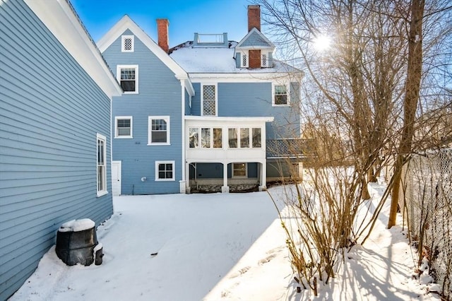 snow covered rear of property featuring a sunroom