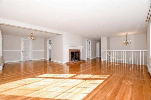 unfurnished living room featuring baseboards, wood finished floors, a chandelier, and a fireplace