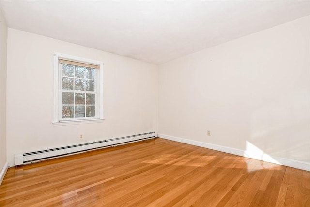 empty room featuring a baseboard heating unit, baseboards, and light wood-style floors