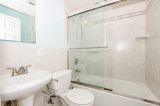 bathroom featuring a sink, wainscoting, tile walls, toilet, and combined bath / shower with glass door