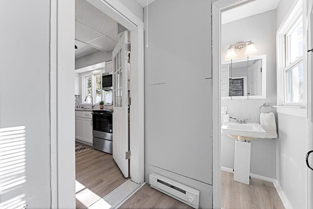 hall featuring a drop ceiling, sink, light hardwood / wood-style flooring, and baseboard heating