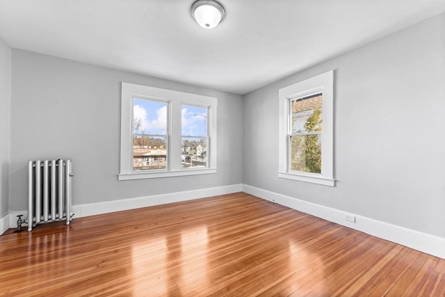 spare room featuring a wealth of natural light, radiator heating unit, and wood-type flooring