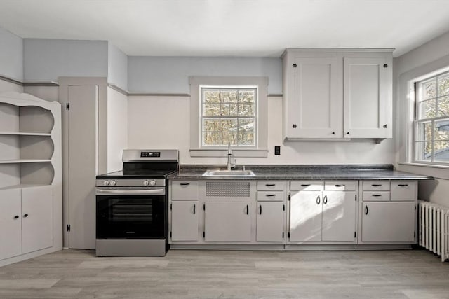 kitchen with white cabinets, radiator heating unit, sink, stainless steel range with electric stovetop, and light wood-type flooring