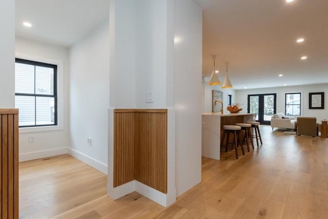 hall with light wood-type flooring, a wealth of natural light, and french doors