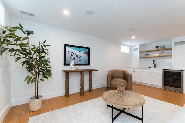 sitting room with light hardwood / wood-style floors, indoor wet bar, and beverage cooler