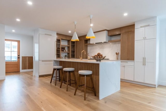 kitchen featuring sink, an island with sink, white cabinetry, and light wood-type flooring