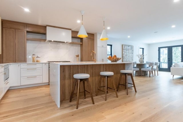 kitchen featuring white cabinets, light wood-type flooring, a center island with sink, and backsplash