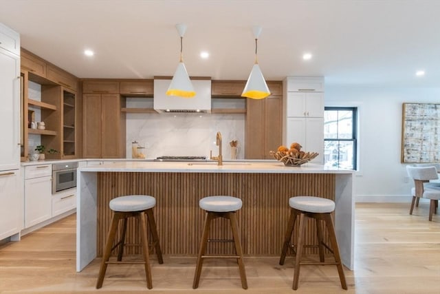 kitchen with light hardwood / wood-style floors, sink, a center island with sink, and tasteful backsplash