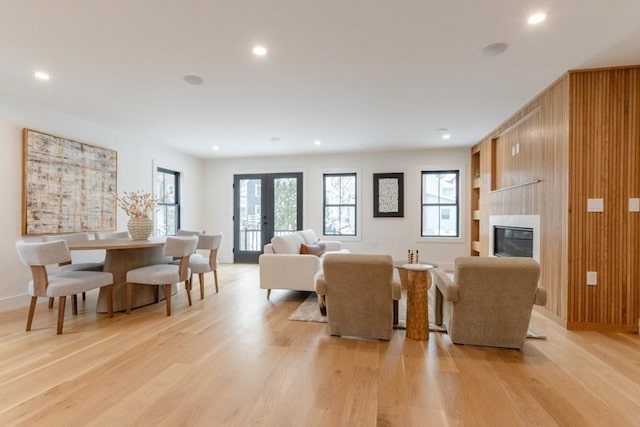 living room with a large fireplace, light hardwood / wood-style floors, wooden walls, and french doors