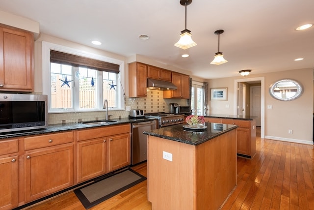 kitchen featuring sink, appliances with stainless steel finishes, hanging light fixtures, backsplash, and a center island