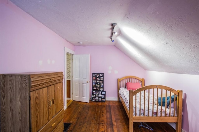 unfurnished bedroom with a textured ceiling, track lighting, vaulted ceiling, and dark wood-type flooring