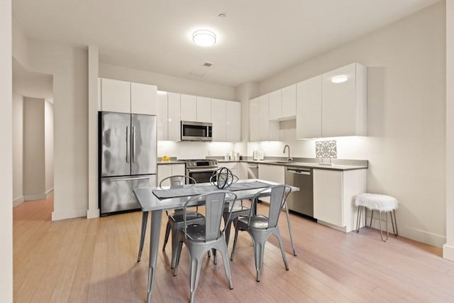 kitchen with white cabinets, appliances with stainless steel finishes, light hardwood / wood-style floors, and sink