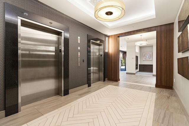 hallway featuring light wood-type flooring, elevator, and a tray ceiling