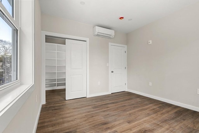 unfurnished bedroom featuring a wall mounted air conditioner, a closet, baseboards, and wood finished floors