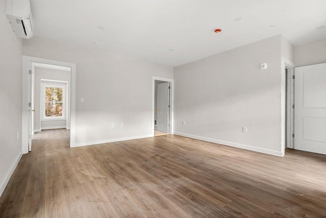 spare room with baseboards, wood finished floors, and an AC wall unit
