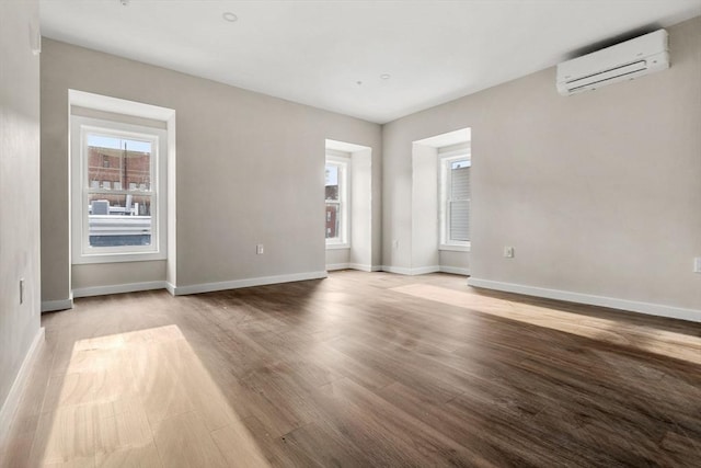 spare room with baseboards, wood finished floors, and a wall unit AC