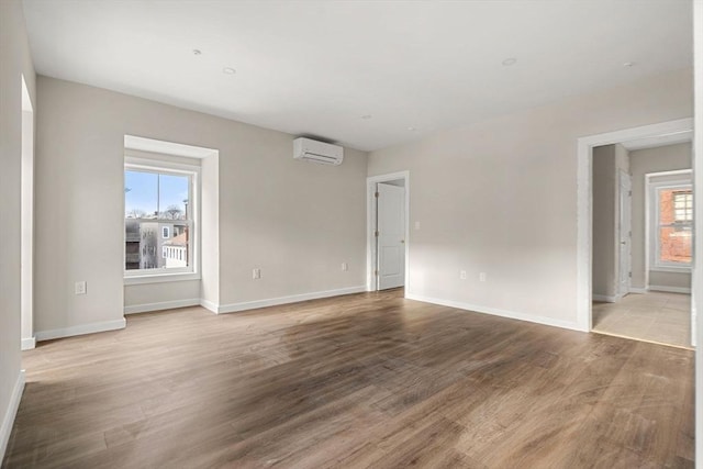 empty room with a wall mounted air conditioner, baseboards, and wood finished floors