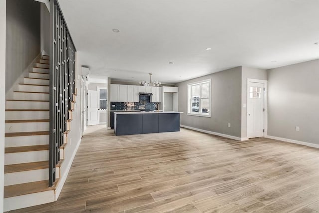 unfurnished living room featuring a chandelier, light wood-style floors, stairway, and baseboards
