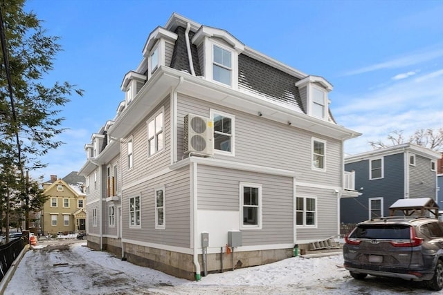snow covered property with a shingled roof and mansard roof