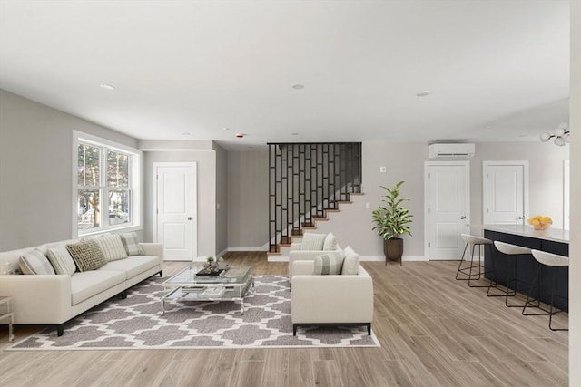 living area featuring a wall mounted air conditioner, baseboards, stairway, and light wood-type flooring