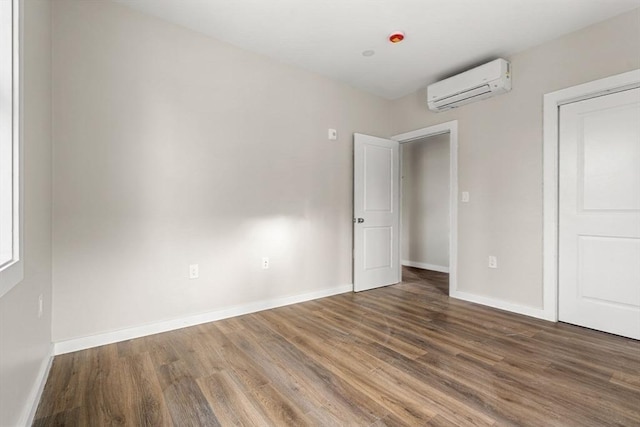 unfurnished bedroom with baseboards, wood finished floors, and an AC wall unit