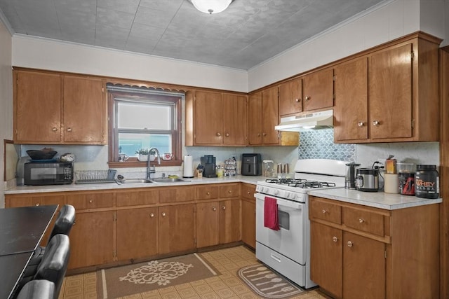 kitchen with brown cabinetry, white gas stove, a sink, light countertops, and under cabinet range hood