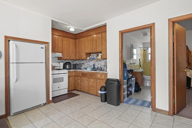 kitchen with under cabinet range hood, tasteful backsplash, white appliances, brown cabinetry, and light countertops