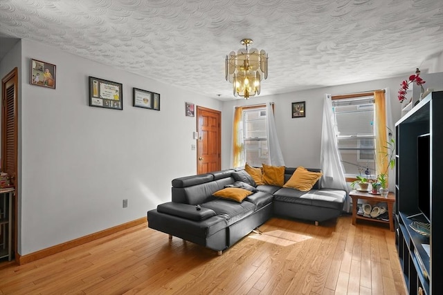 living room with a notable chandelier, baseboards, light wood-type flooring, and a textured ceiling