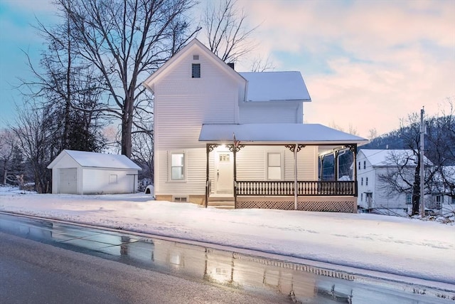 snow covered back of property with an outbuilding, a porch, and a detached garage