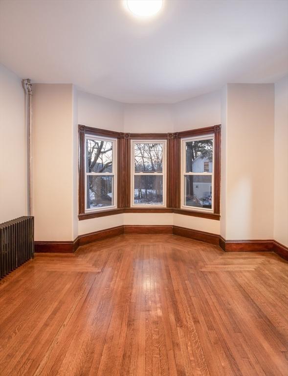 spare room with radiator heating unit, light wood-style flooring, and baseboards