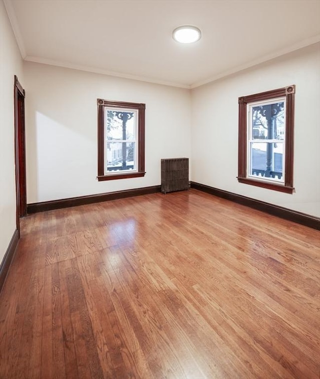 spare room with ornamental molding, radiator, baseboards, and wood finished floors