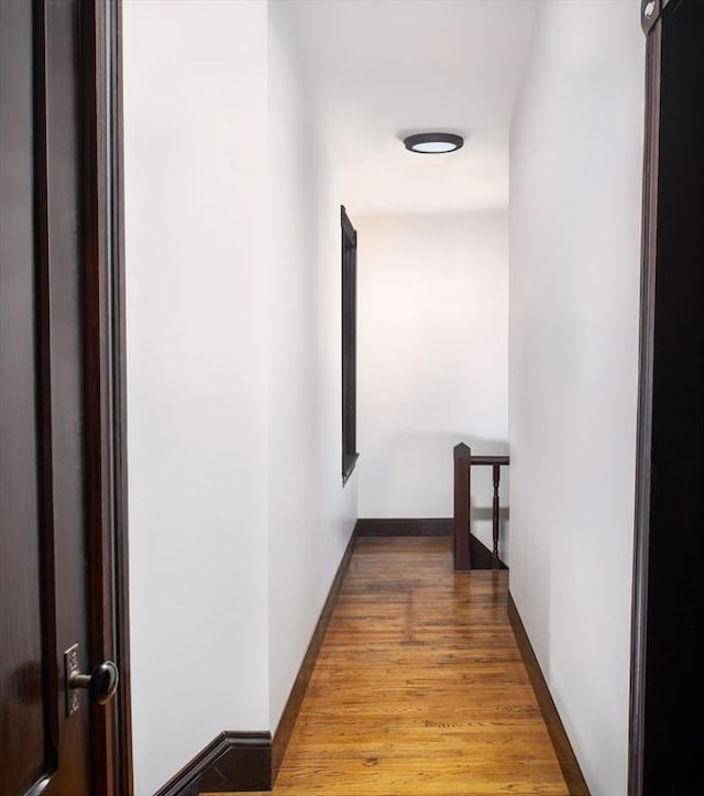 hallway with baseboards, an upstairs landing, and wood finished floors