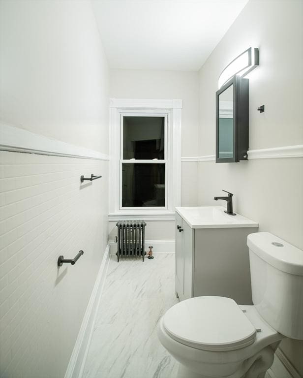 half bath featuring baseboards, toilet, radiator heating unit, marble finish floor, and vanity