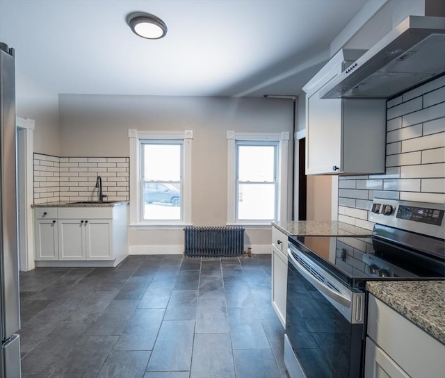 kitchen featuring wall chimney exhaust hood, radiator heating unit, stainless steel electric range, white cabinetry, and backsplash