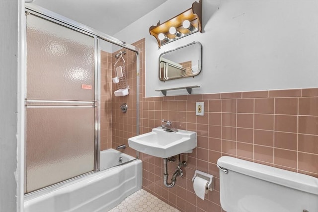 full bathroom featuring bath / shower combo with glass door, sink, tile walls, toilet, and tile patterned floors