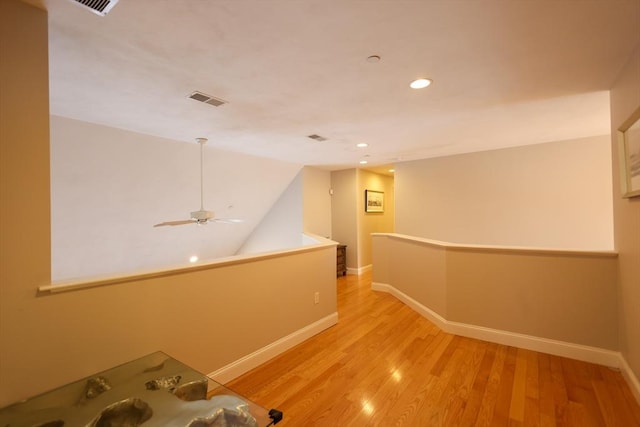 hallway featuring light wood-style floors, baseboards, visible vents, and an upstairs landing