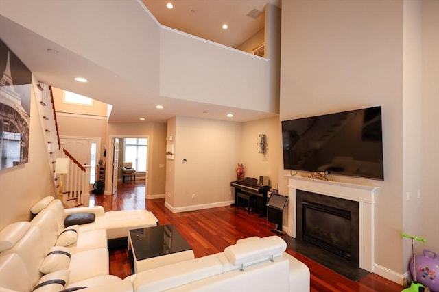 living area featuring recessed lighting, wood finished floors, baseboards, stairway, and a glass covered fireplace