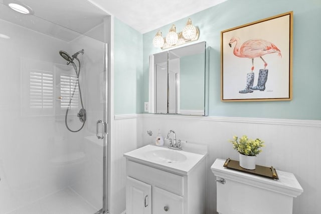 full bath featuring toilet, a stall shower, vanity, and a wainscoted wall