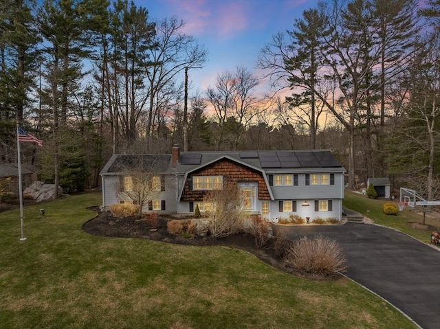 view of front of home featuring a gambrel roof, a front lawn, solar panels, a chimney, and driveway