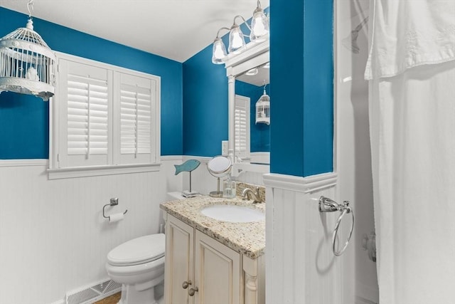 bathroom featuring toilet, visible vents, a wainscoted wall, and vanity