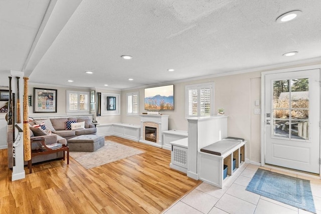 living room featuring a fireplace, light wood finished floors, a textured ceiling, and ornamental molding