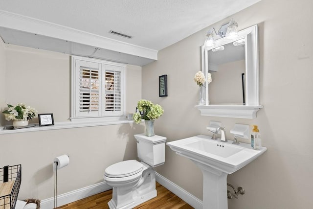 half bathroom with a textured ceiling, visible vents, toilet, wood finished floors, and baseboards