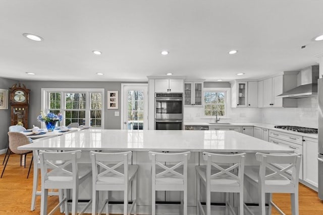 kitchen with light wood-style floors, wall chimney exhaust hood, a center island, stainless steel appliances, and backsplash