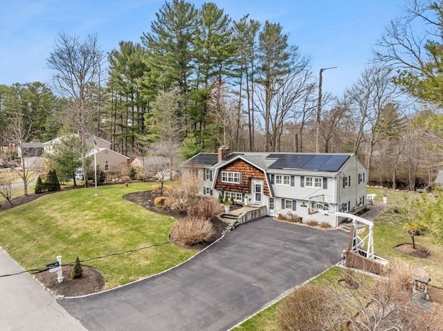 view of front of property featuring a front yard, solar panels, a chimney, aphalt driveway, and a gambrel roof