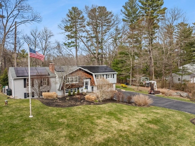 back of property featuring a chimney, roof mounted solar panels, driveway, and a lawn